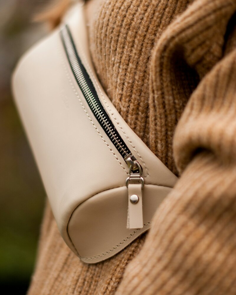 The Sling — cream leather sling bag worn over a camel knit